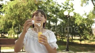 小女孩在公园里玩，把泡泡吹进镜头。 慢动作。 漂亮的女孩吹肥皂